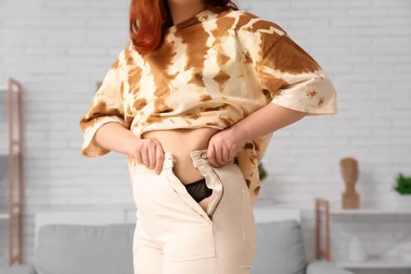 Image of woman trying to do her trousers up after pregnancy weight gain Virginia Water