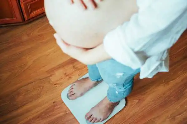 Image of woman weighing herself and experiencing weight gain through pregnancy Virginia Water